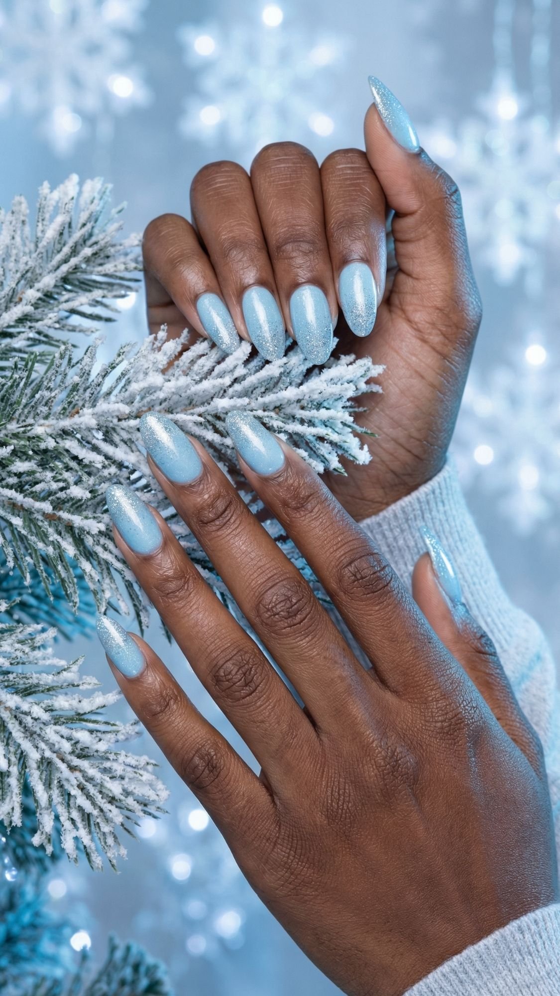 A person with shimmering light blue, almond-shaped nails gently touches a frosted pine branch, with a soft blue background featuring snowflake decorations—perfect elegant nails for chic nail ideas at holiday parties.