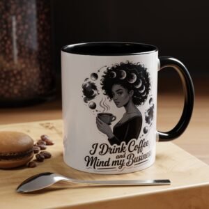 A coffee mug with a black handle features an illustration of a woman holding a cup, surrounded by moons, and the text I Drink Coffee and Mind my Business—perfect for any introvert looking to recharge. A spoon, macaron, and coffee beans rest nearby.