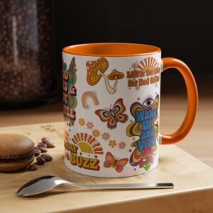 A colorful mug with orange handle and rim sits on a wooden surface. Featuring retro designs and phrases like “Wake Up and Vibe,” it’s perfect for an introvert’s fall reset. A spoon and macaron sit nearby, inviting you to relax and recharge.