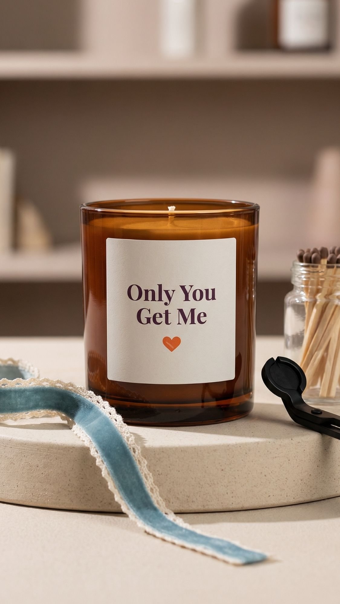 A brown glass candle labeled Only You Get Me, perfect for handmade birthday gifts, sits on a round beige surface. Nearby are a blue ribbon, a jar of matches, and a black candle snuffer.