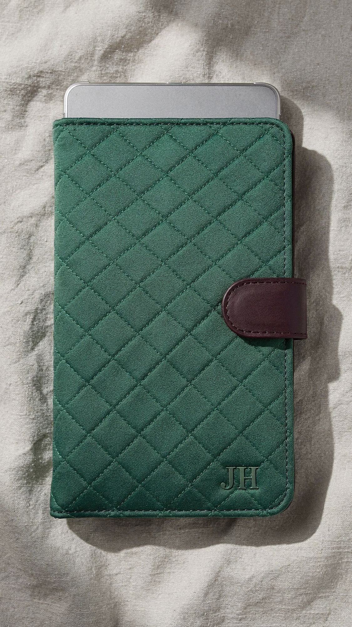 A green quilted tablet cover with a brown strap and the initials JH embossed in the lower right corner, resting on a light fabric surface. The top of a silver device peeks out—perfect as one of those unique handmade gifts for your best friend.