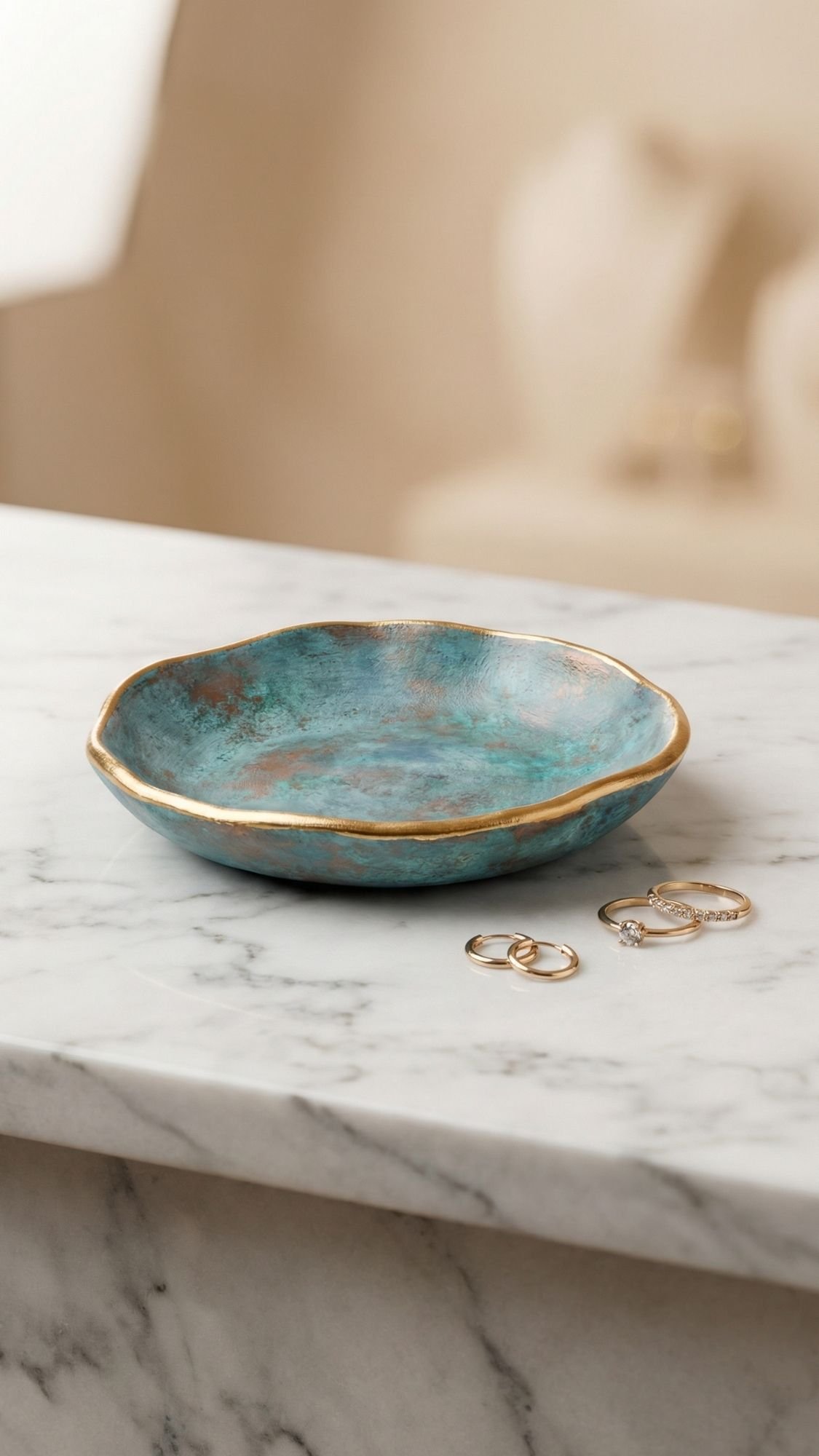 A shallow, round, turquoise and gold-rimmed ceramic dish sits on a white marble surface with a few gold rings placed beside it—perfect for easy handmade gifts or as thoughtful birthday gifts for best friend. The background is softly blurred.