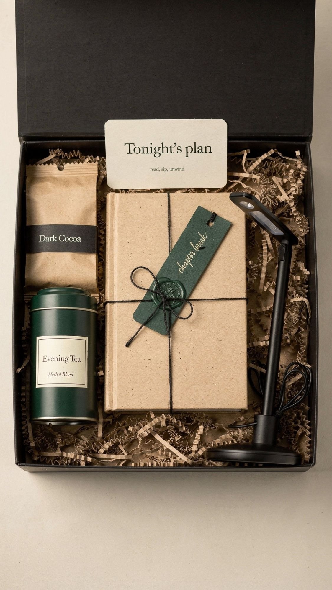 A charming winter gift set featuring a brown-wrapped journal, evening herbal tea, dark cocoa, a candle holder with snuffer, and a card reading “Tonight’s plan: read, sip, unwind.” Perfect for cozy winter nights.