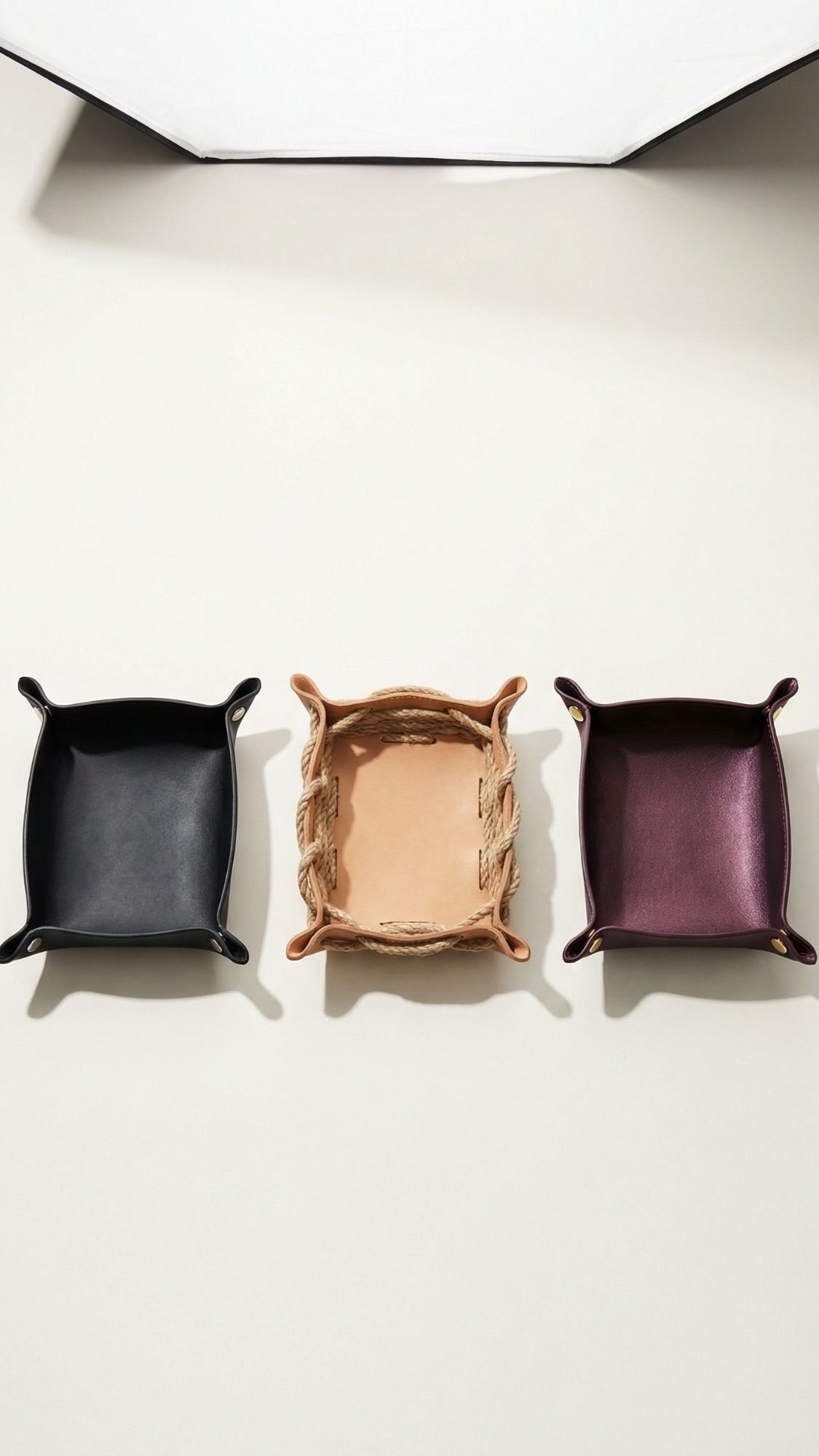 Three square trays are arranged side by side: a black tray on the left, a tan woven tray in the center, and a dark purple tray on the right—practical and stylish useful gifts for him, perfect as handmade gifts for your boyfriend.