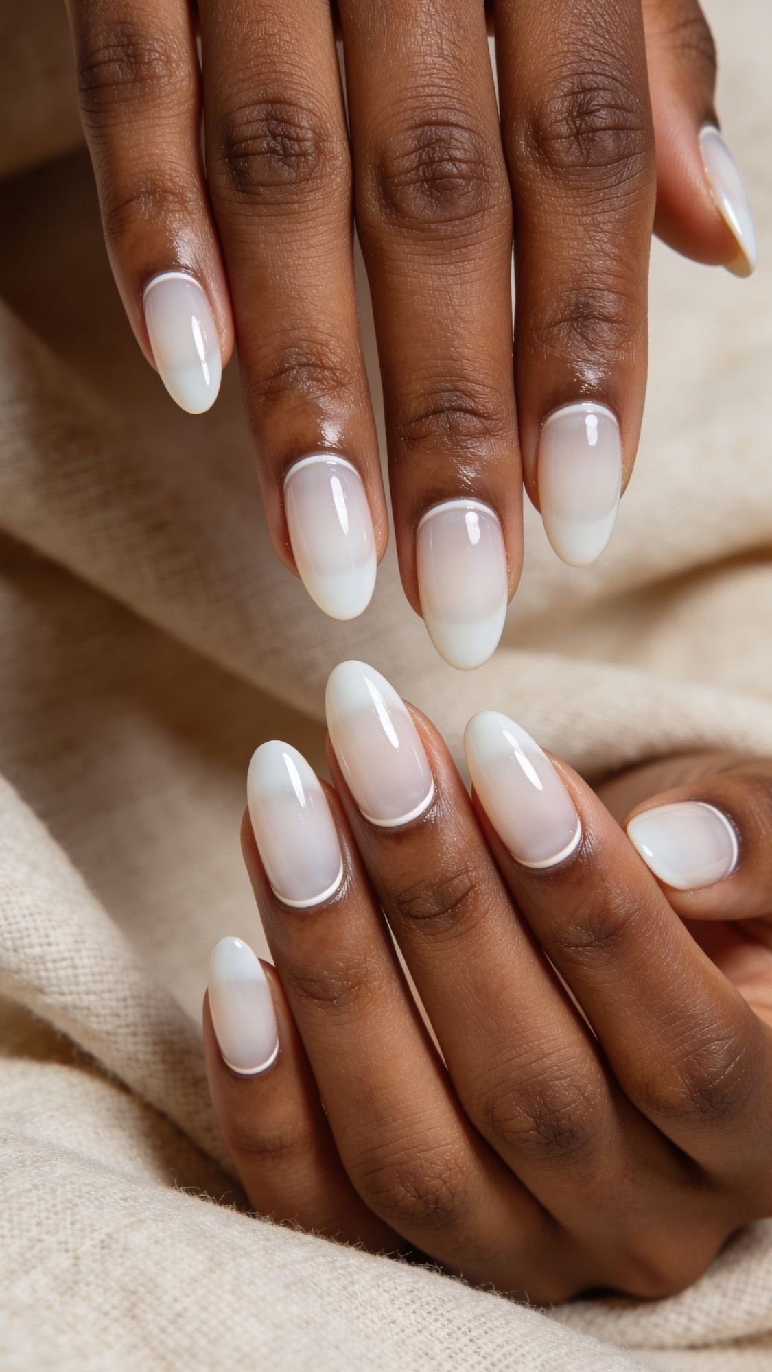 Close-up of hands with neatly manicured, polished nails painted in a glossy, semi-transparent milky white shade, perfect for a clean girl nails everyday look, resting on light beige textured fabric.