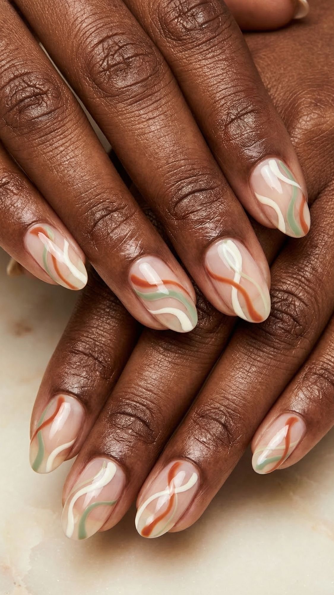 A close-up of hands with almond-shaped nails featuring a nude base and abstract wavy lines in white, olive green, and terracotta colors—perfect inspiration for easy nail designs you can try on your simple nails at home. The glossy finish adds a polished touch.