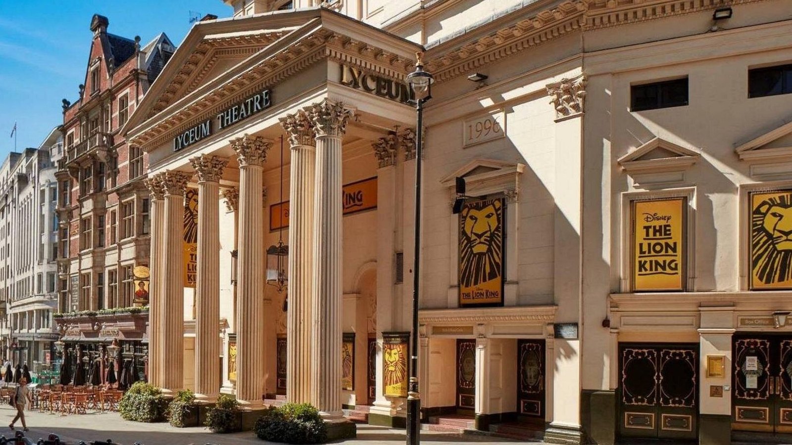 The exterior of the Lyceum Theatre in London, a must-see among London attractions, features tall columns and posters for Disney’s “The Lion King” musical. The quiet street outside is lined with other historic buildings.