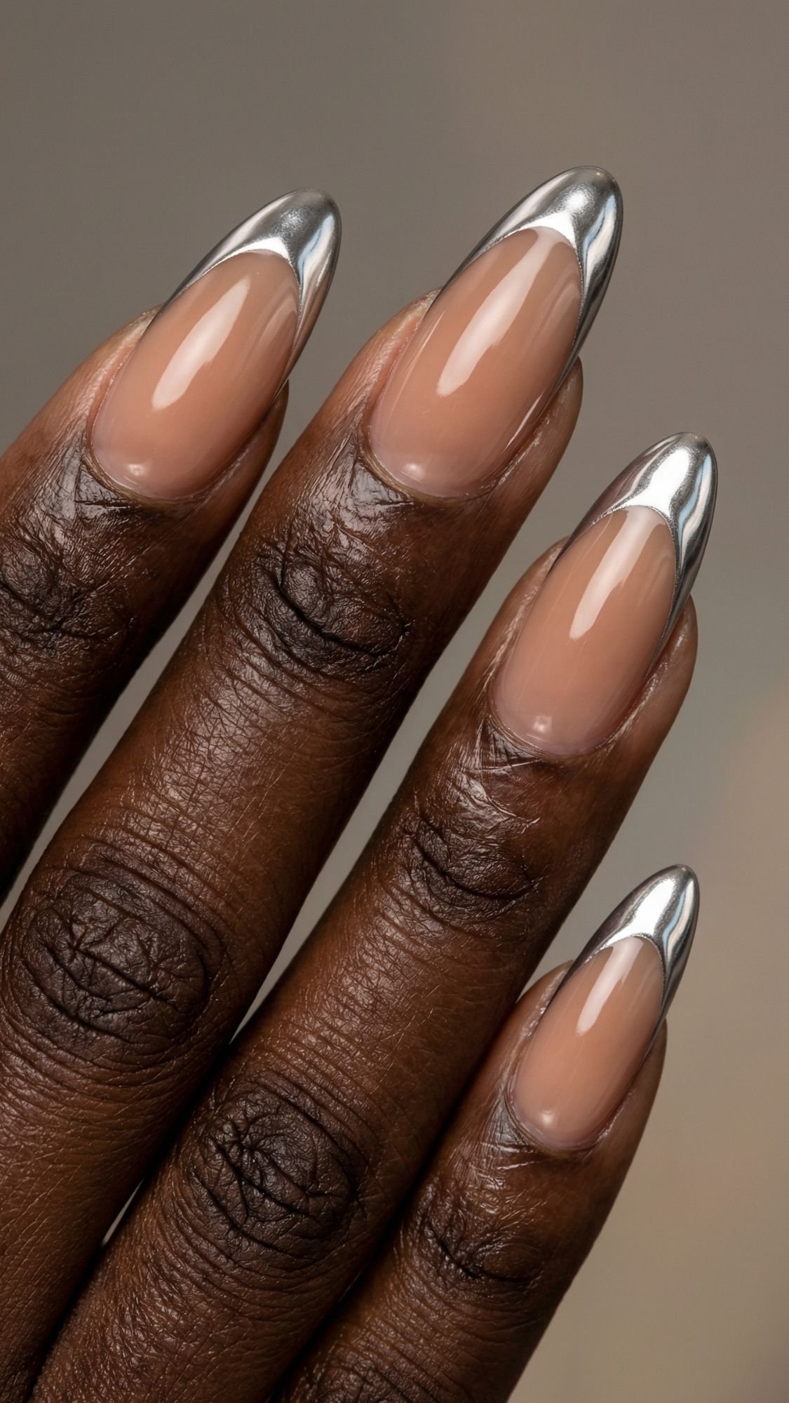 A close-up of a hand with almond-shaped nails featuring a nude base and shiny silver chrome tips, creating an easy nail design for a modern, metallic French manicure style that’s perfect for simple nails you can do at home.