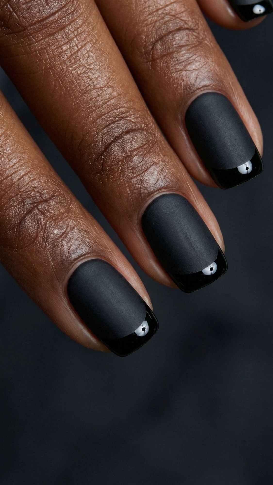A close-up of fingers with square-shaped black nails featuring a matte finish and glossy black tips, showing a modern French manicure style—perfect inspiration for easy nail designs you can try on your nails at home.