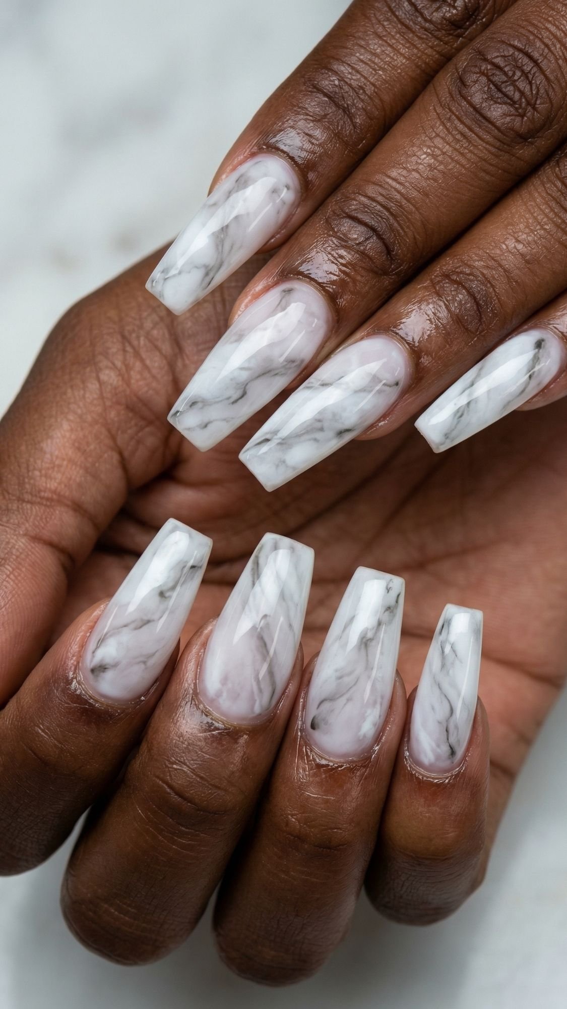 A close-up of hands with long, coffin-shaped nails featuring a glossy white and gray marble design. The natural skin tone provides contrast to this elegant manicure—perfect inspiration for simple nails or easy nail designs you can try at home.