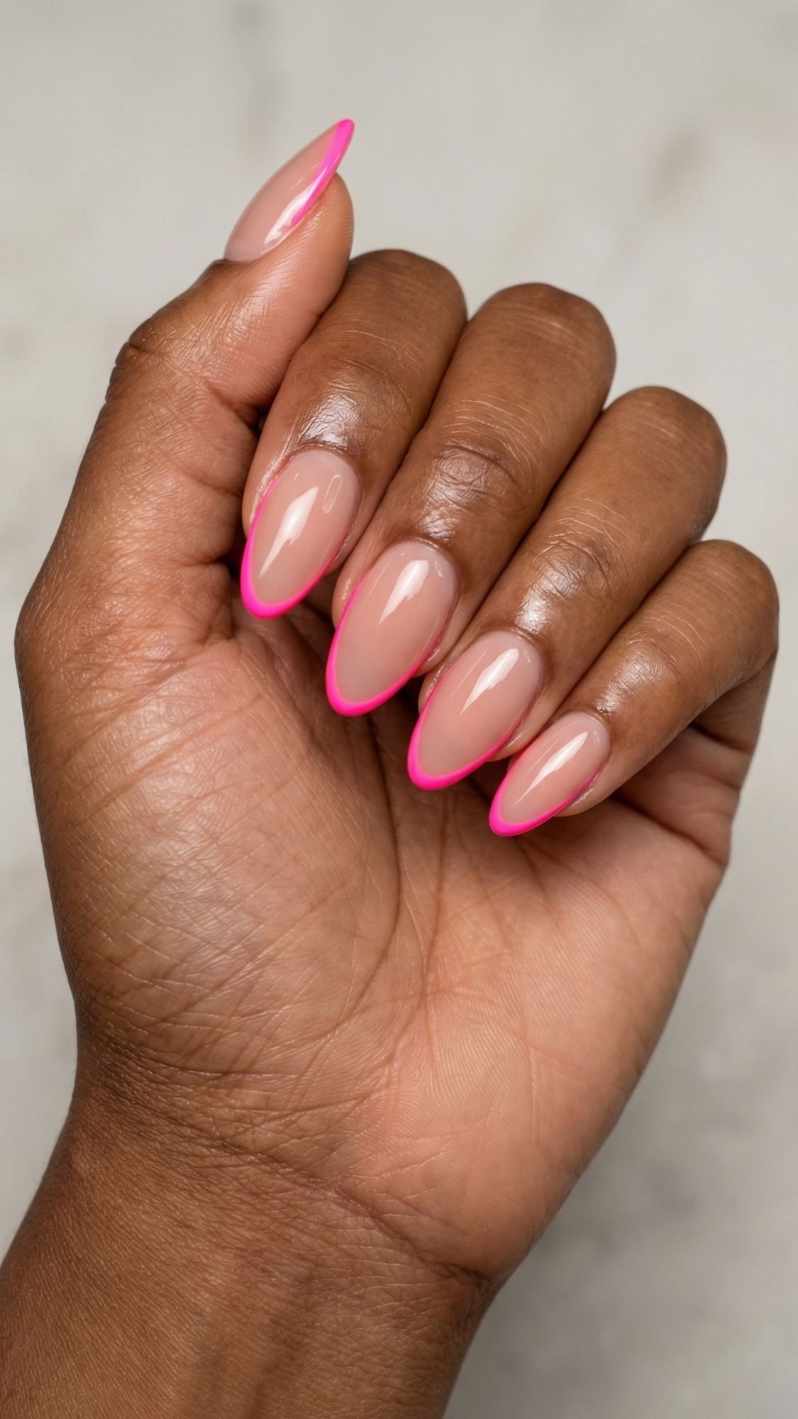 A hand with almond-shaped nails polished in glossy nude, each featuring a bright pink French tip—perfect for simple nails or quick nail ideas you can easily recreate as nails at home, all shown against a light, neutral background.