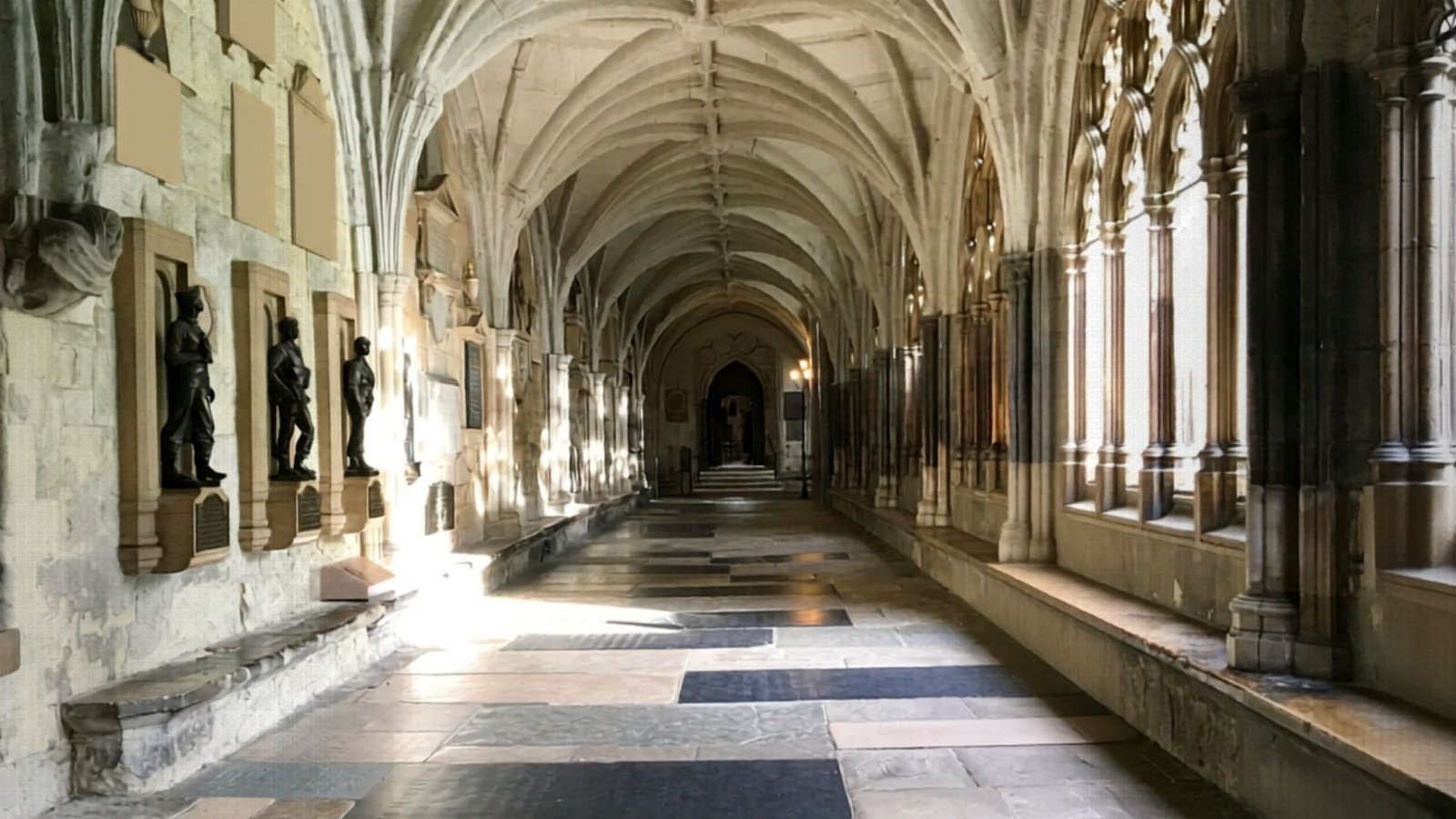 A long, arched stone corridor with high vaulted ceilings, statues in alcoves on the left wall, and large windows on the right letting in sunlight—a must-see spot for your first trip London and those seeking unique London things to do.