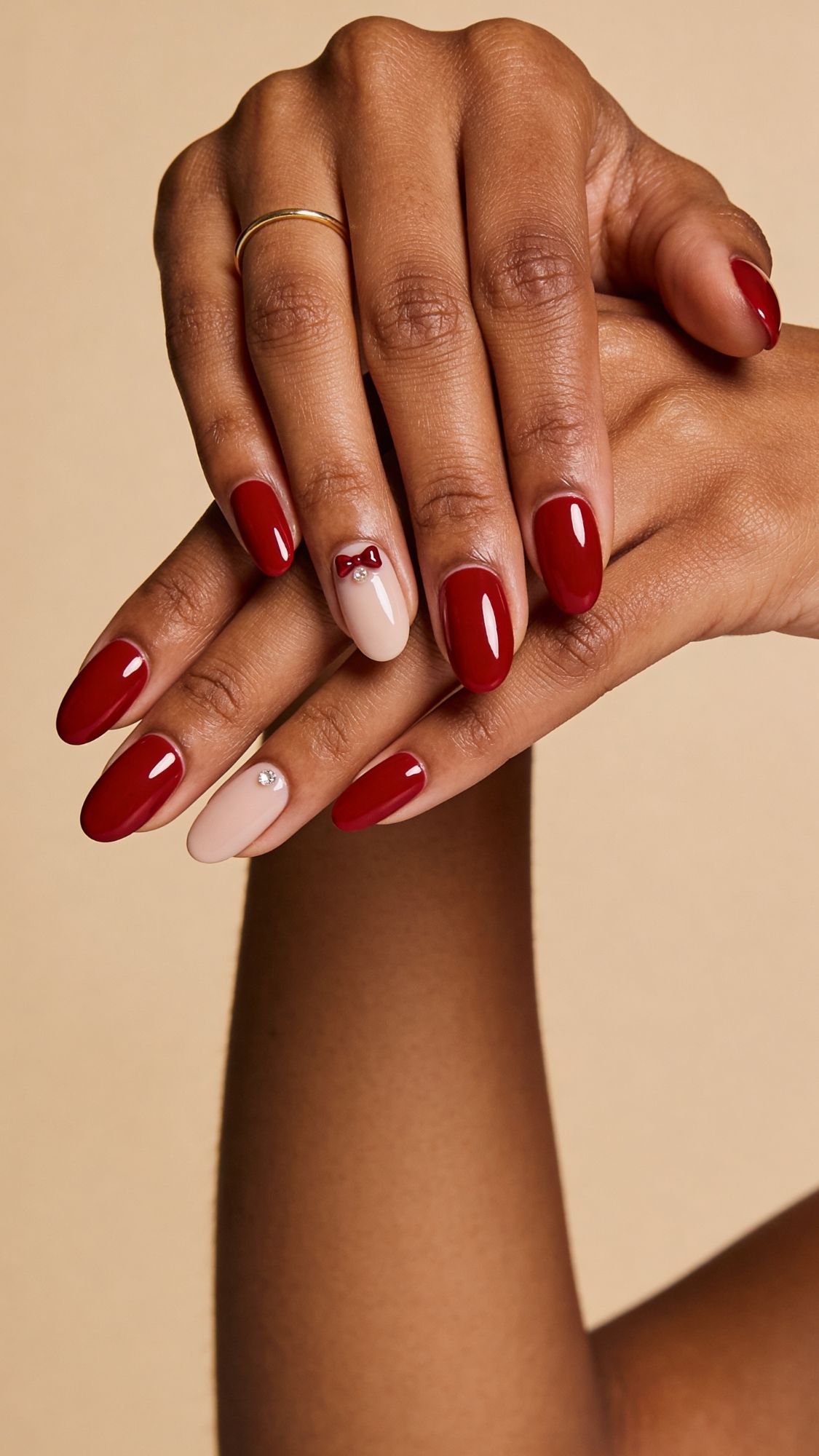 Showcasing chic red nails, this manicure features glossy red polish on most fingers, with unique nail ideas for every season—a nude ring finger accented by a tiny red bow on one hand and a small pearl-like bead on the other.