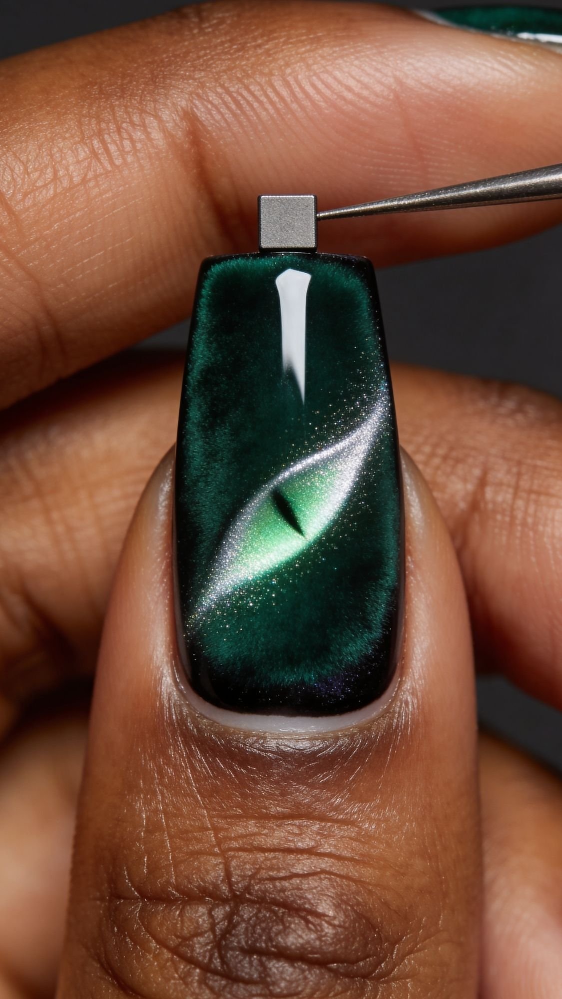 A close-up of a fingernail painted with dark green polish features a detailed cat or reptile eye design, complete with a slit-shaped pupil and metallic sheen—perfect inspiration for DIY nails or bold yet simple nails created at home.