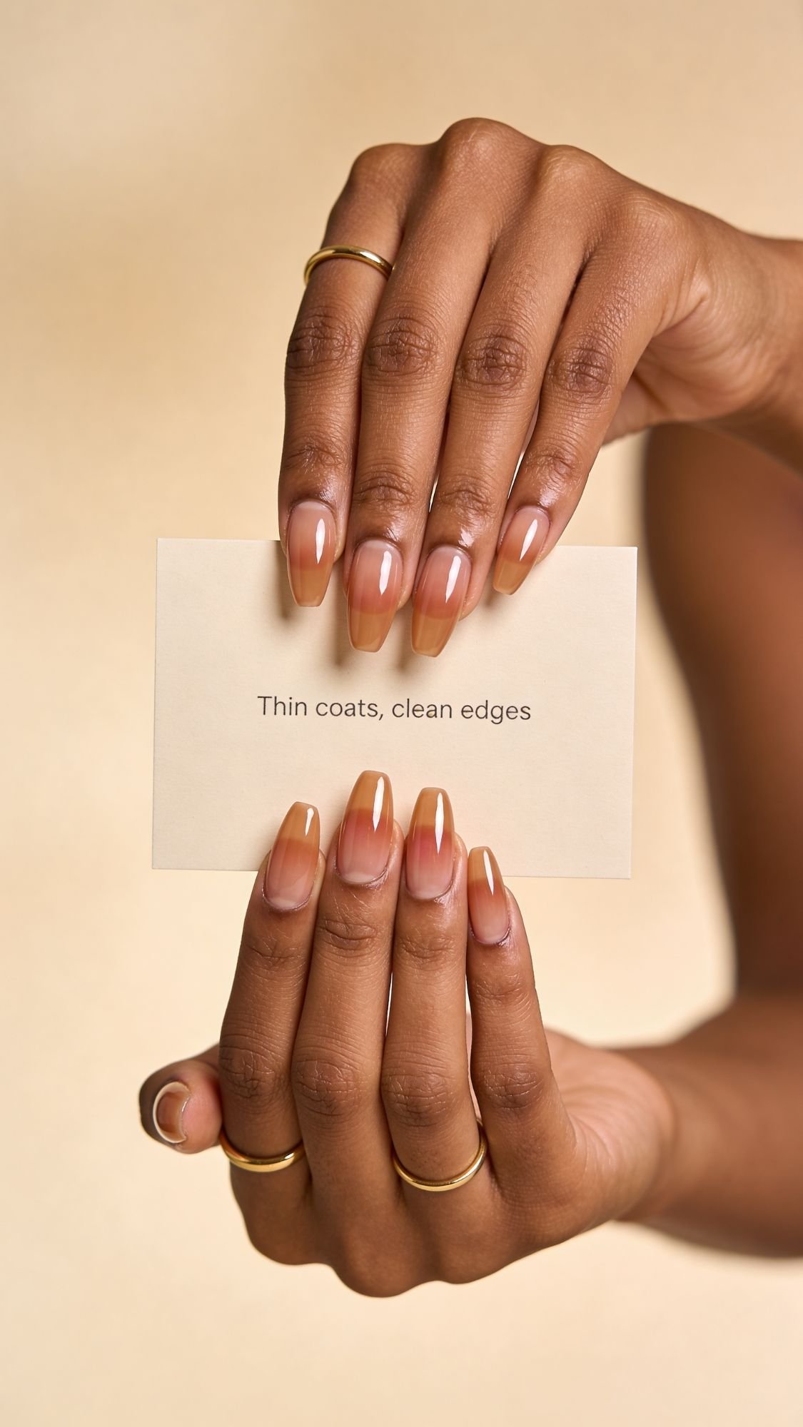 A person with a fresh, natural ombre manicure—perfect for spring nails—holds a card that reads Thin coats, clean edges. Their hands, adorned with gold rings, stand out beautifully against a neutral background.