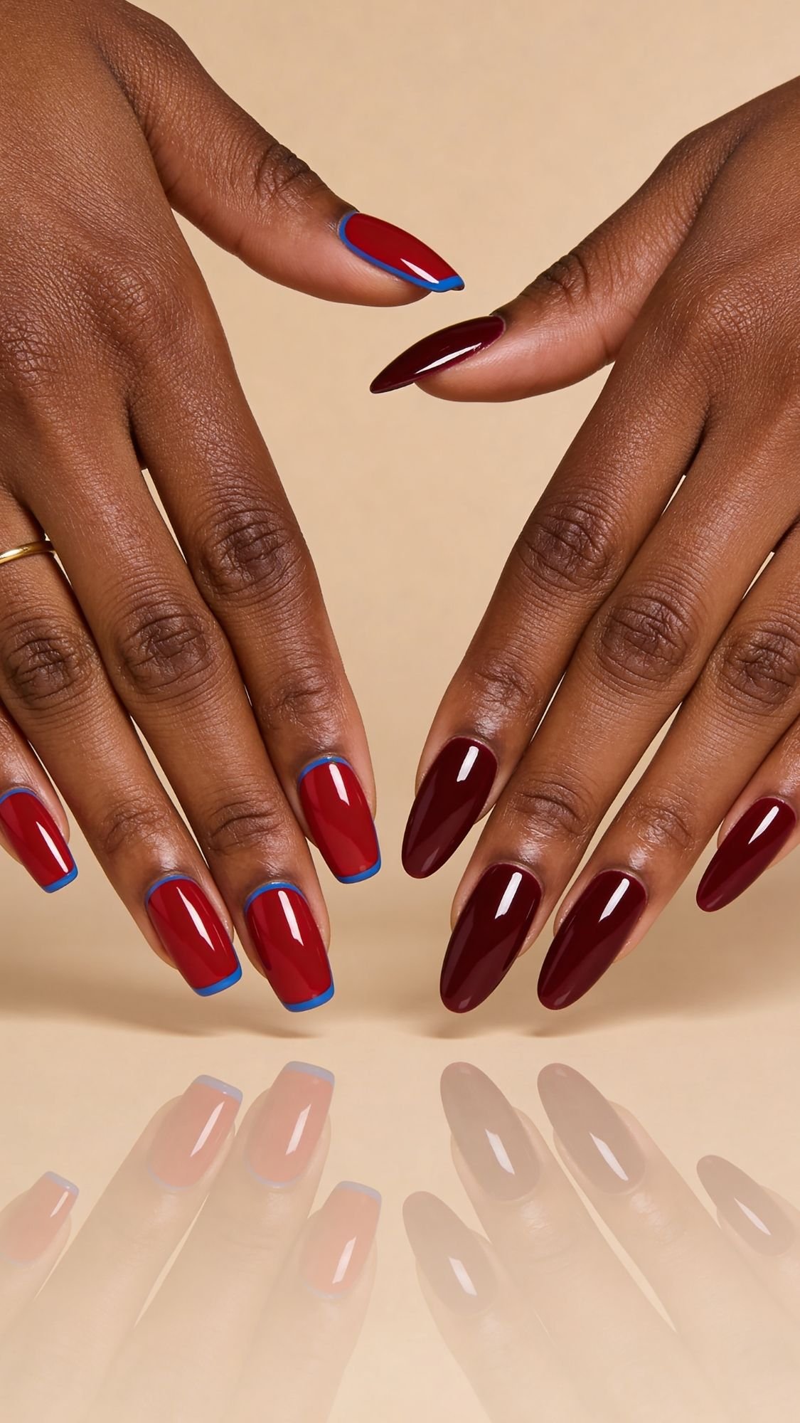 Two hands with dark skin display manicured red nails, some tipped with a subtle blue outline—perfect inspiration for seasonal nails. The beige background and reflected nails add an elegant touch to these creative nail ideas.