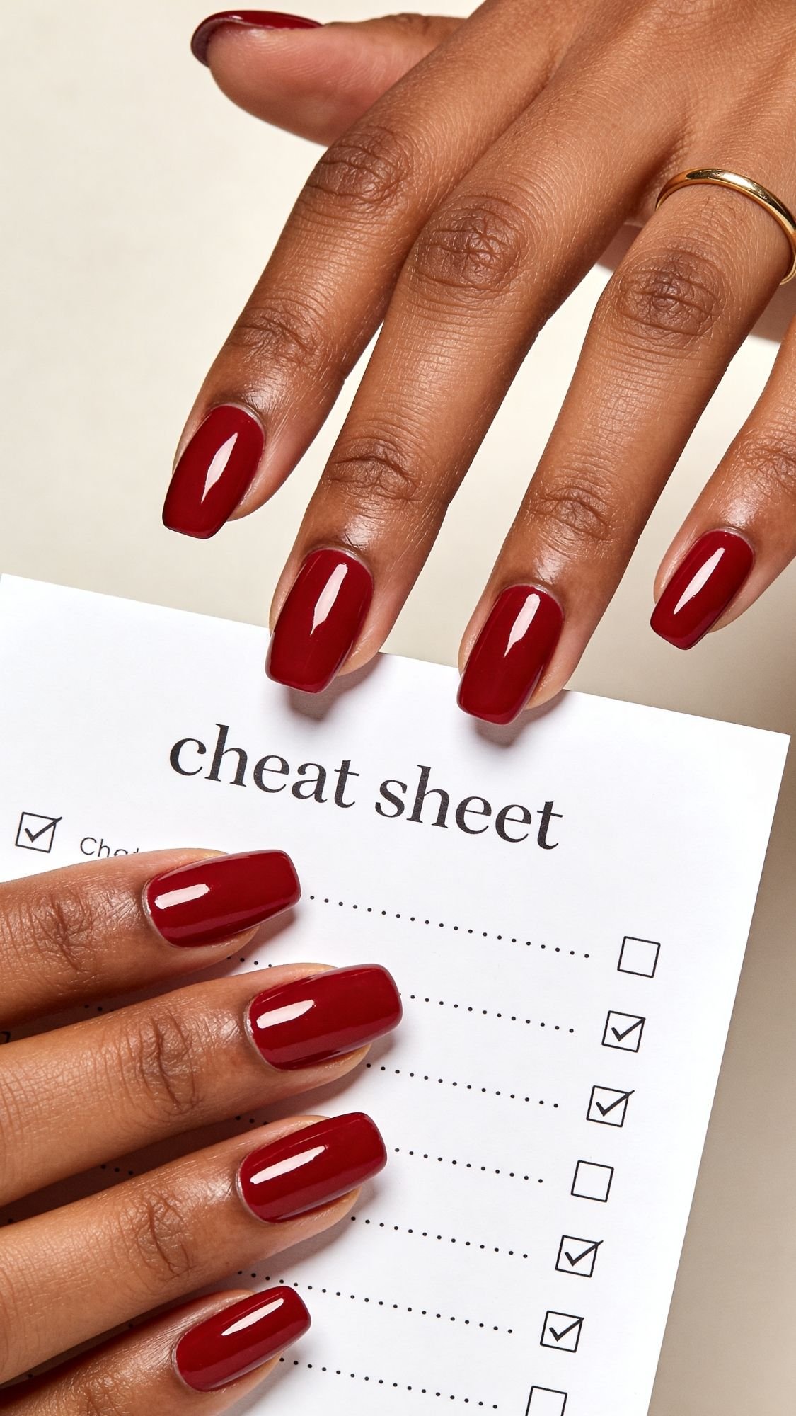 A person with neatly manicured red nails, perfect for every season, holds a paper titled cheat sheet with a checklist, while their other hand rests on the page. The person wears a simple gold ring.