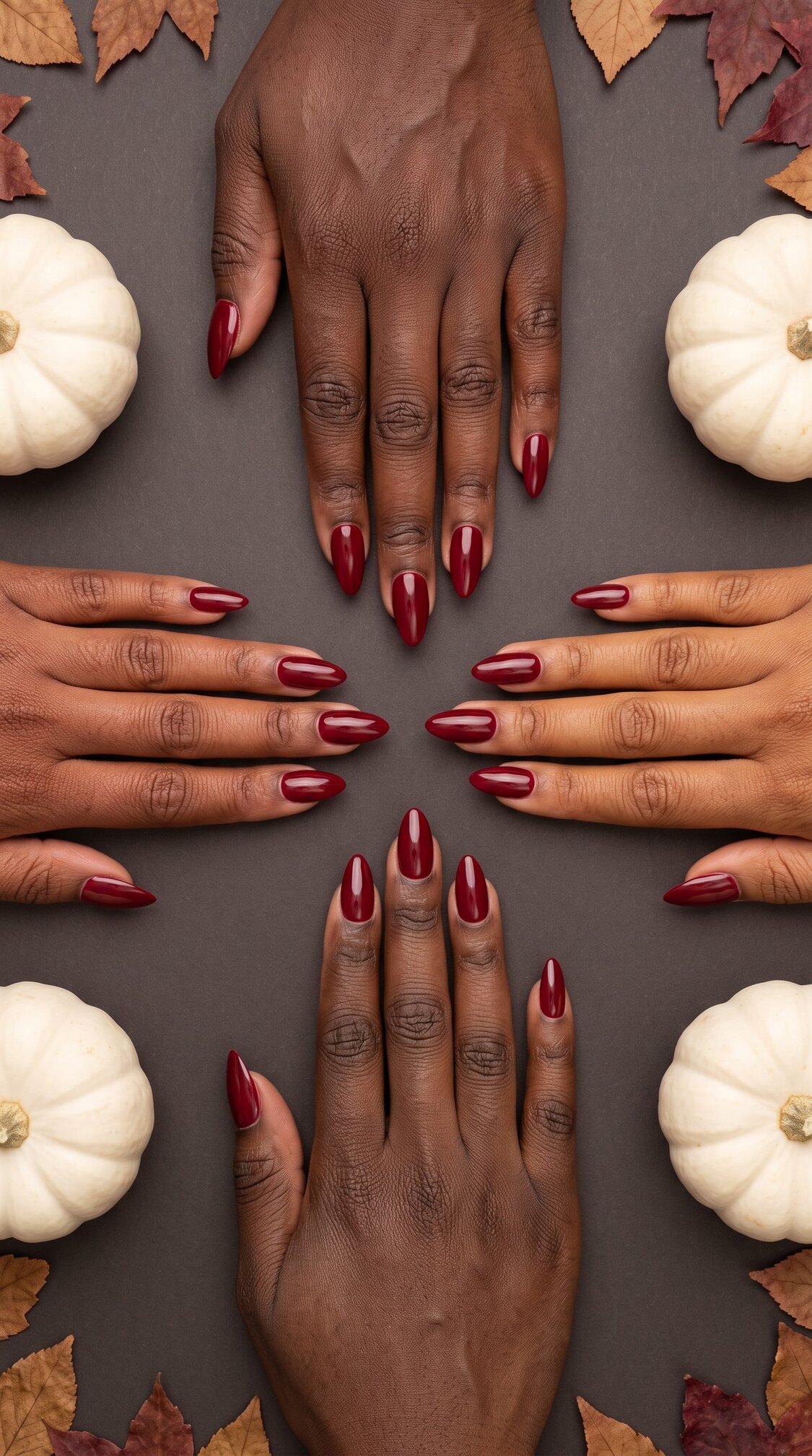 Four hands with dark skin and dark red halloween nails acrylic are arranged symmetrically on a dark surface, surrounded by white pumpkins and autumn leaves.