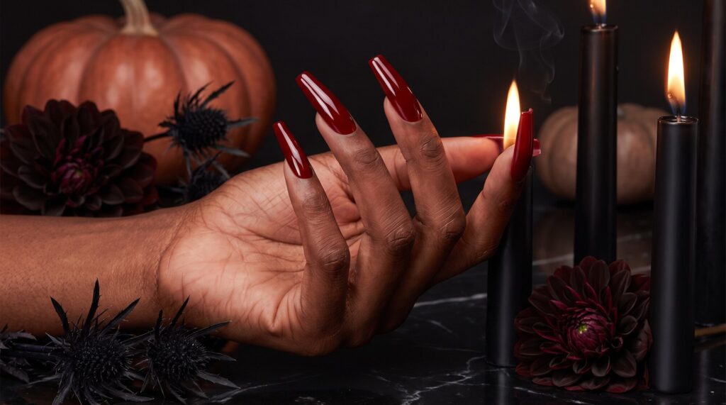 Long blood red coffin acrylic nails on deep espresso skin, lit by black taper candles beside dark dahlias on black marble.