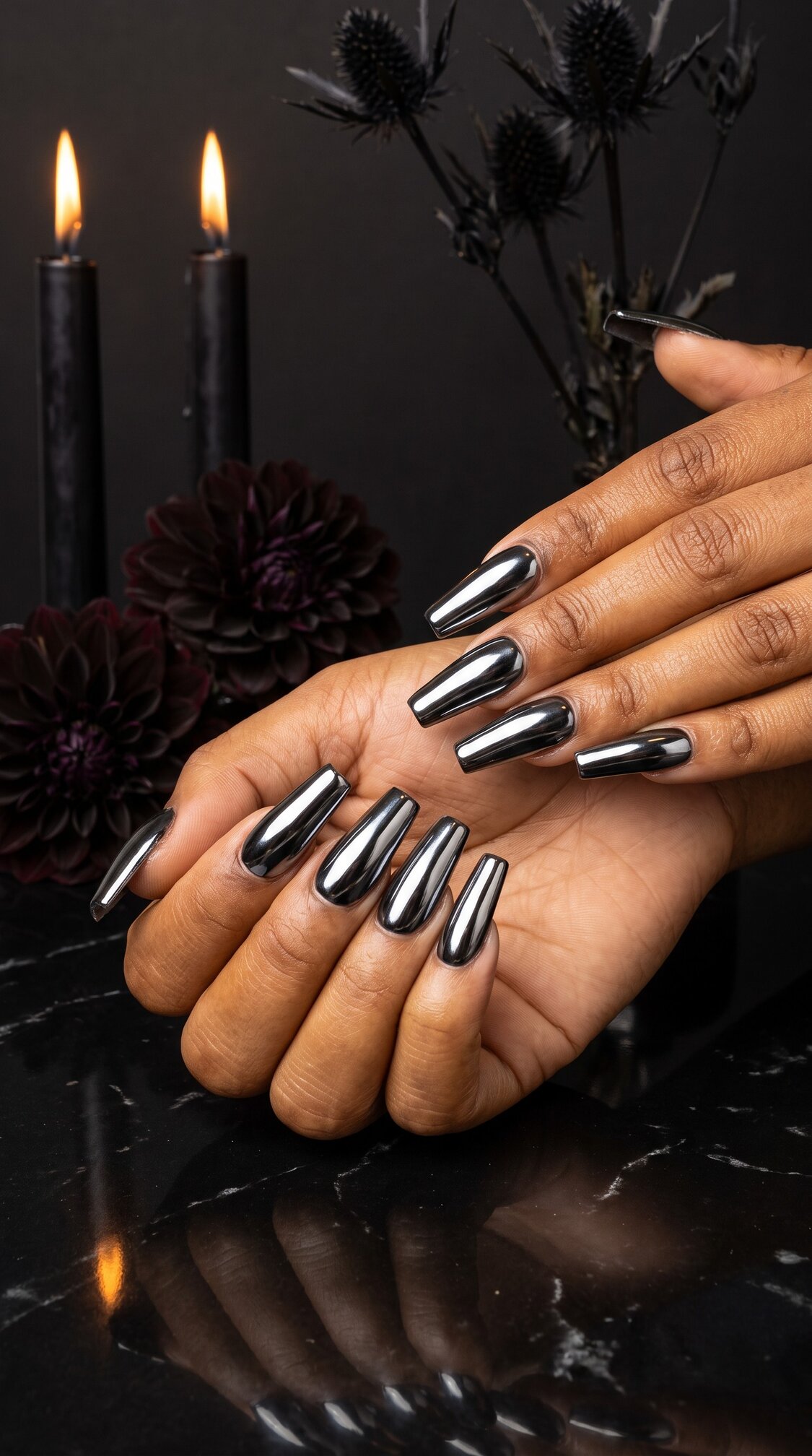 Hands with long, shiny black chrome halloween nails acrylic are displayed against a dark background with black candles, dark flowers, and moody lighting, creating an elegant and dramatic look.